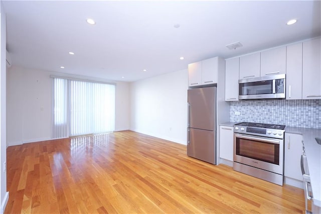 kitchen with tasteful backsplash, white cabinets, light wood-type flooring, and appliances with stainless steel finishes