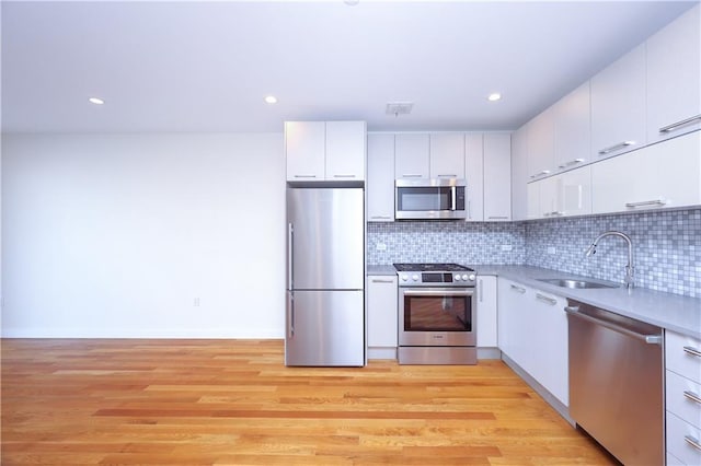 kitchen with white cabinets, sink, stainless steel appliances, and light hardwood / wood-style flooring