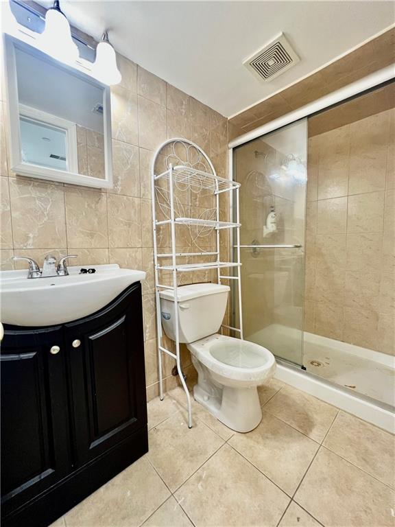 bathroom featuring a shower with shower door, tile walls, tile patterned flooring, vanity, and toilet