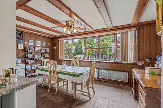 dining room with beam ceiling, wood walls, and ceiling fan