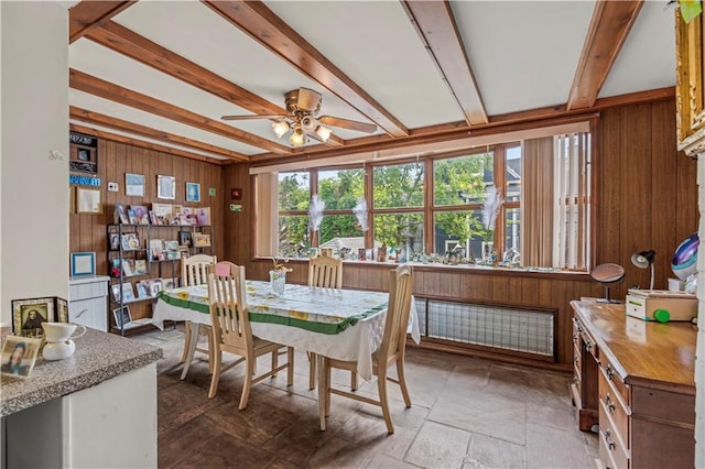 dining space with beam ceiling, ceiling fan, and wooden walls