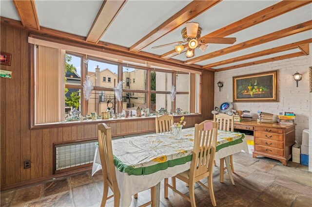 dining room with wood walls, beamed ceiling, ceiling fan, and brick wall