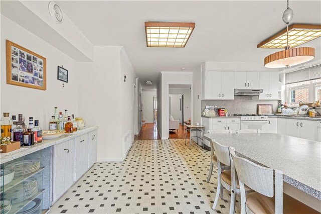 kitchen with decorative backsplash, pendant lighting, white stove, and white cabinetry