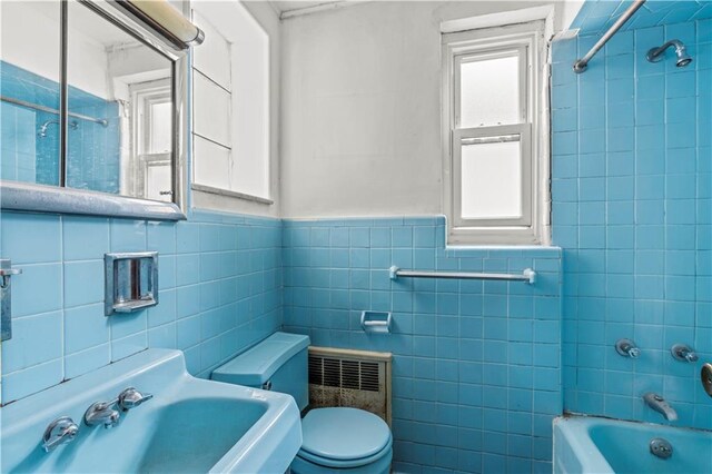 full bathroom with sink, tiled shower / bath, tile walls, and toilet