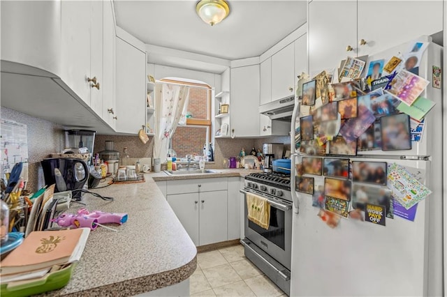 kitchen with sink, light tile patterned floors, stainless steel gas range, refrigerator, and white cabinets