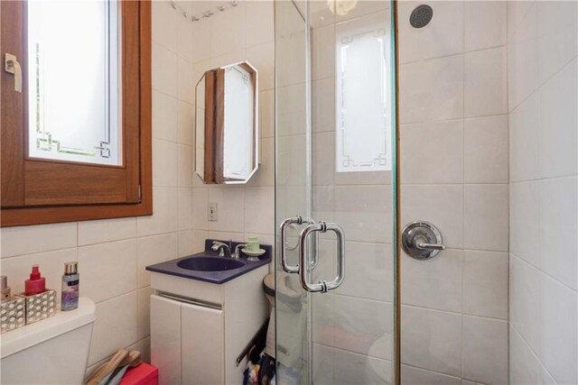 bathroom with tile walls, decorative backsplash, vanity, an enclosed shower, and toilet