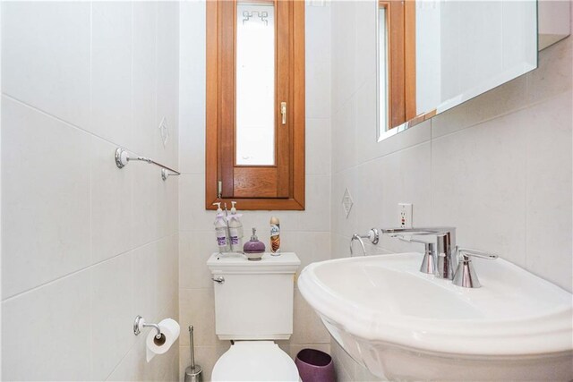 bathroom with sink, tile walls, and toilet