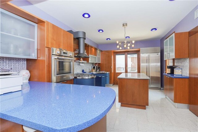 kitchen with appliances with stainless steel finishes, pendant lighting, island exhaust hood, a center island, and a notable chandelier