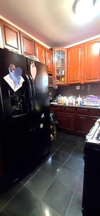 2319 W 12th St, Brooklyn, NY 11223 - kitchen with black refrigerator with ice dispenser, dark tile patterned flooring, glass insert cabinets, brown cabinets, and dark countertops