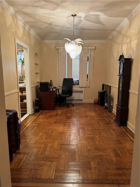 unfurnished office with parquet flooring, crown molding, an inviting chandelier, radiator heating unit, and built in features