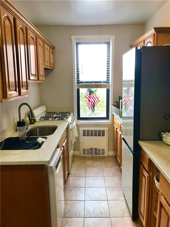 kitchen featuring radiator heating unit, appliances with stainless steel finishes, light stone counters, a sink, and light tile patterned flooring