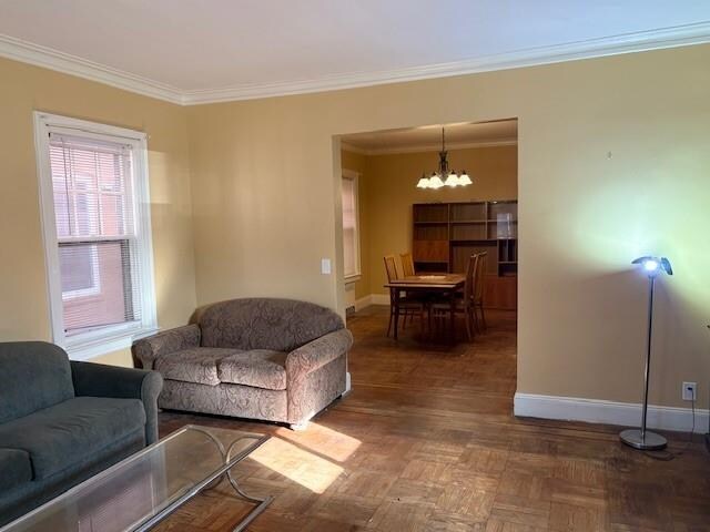 living room featuring a notable chandelier, crown molding, and dark parquet floors