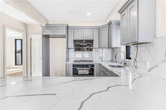 kitchen with gray cabinets, light stone countertops, oven, and a sink