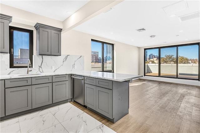 kitchen featuring tasteful backsplash, visible vents, gray cabinetry, a peninsula, and a sink