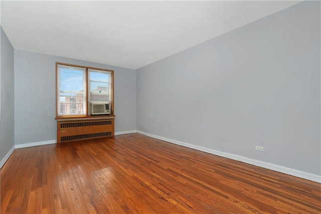 unfurnished room featuring baseboards, cooling unit, hardwood / wood-style flooring, and radiator