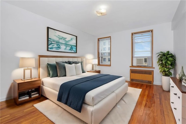 bedroom featuring radiator heating unit, light wood-style flooring, and cooling unit