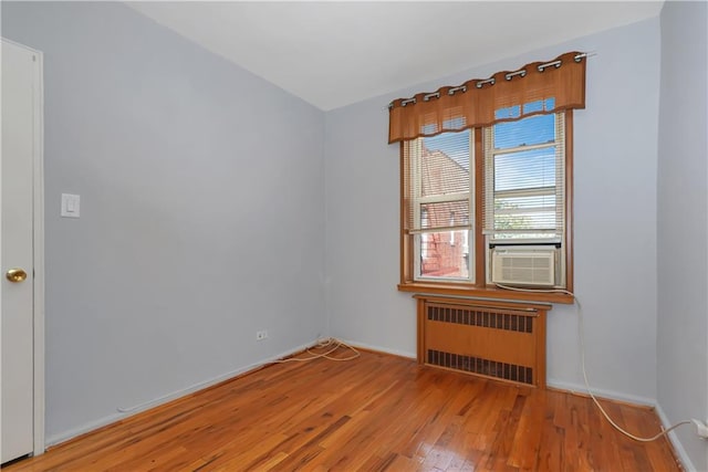 empty room featuring cooling unit, baseboards, light wood finished floors, and radiator heating unit