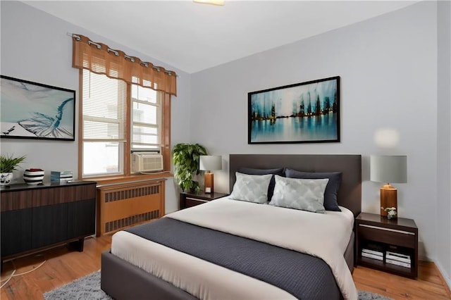 bedroom featuring radiator heating unit, cooling unit, and light wood-style floors