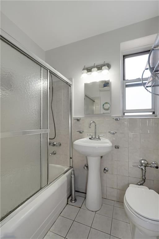 full bathroom featuring wainscoting, toilet, tile patterned floors, combined bath / shower with glass door, and tile walls