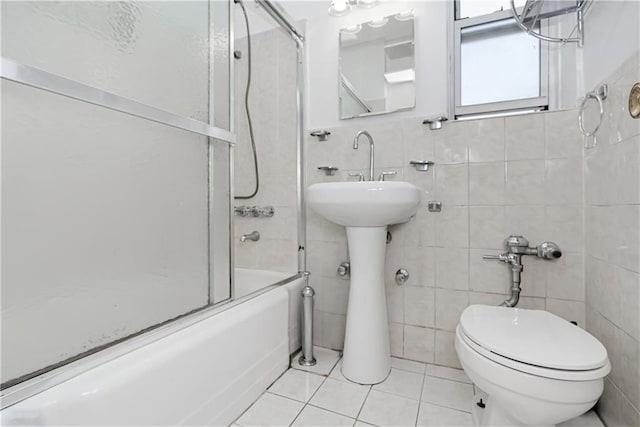 bathroom featuring tile patterned flooring, bath / shower combo with glass door, tile walls, and toilet