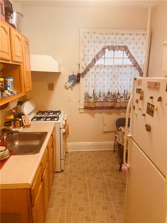 kitchen featuring sink, light tile patterned flooring, white appliances, and premium range hood