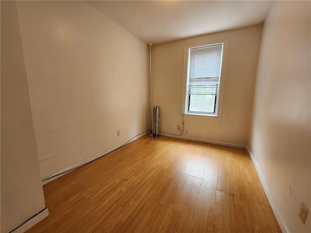 spare room with radiator, light wood-style flooring, and baseboards