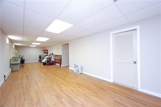 below grade area featuring a baseboard radiator, baseboards, a drop ceiling, and wood finished floors