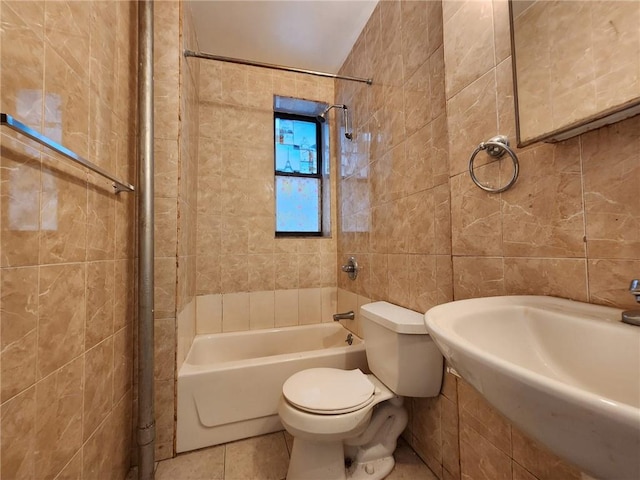 bathroom with tile walls, bathing tub / shower combination, toilet, tile patterned floors, and a sink