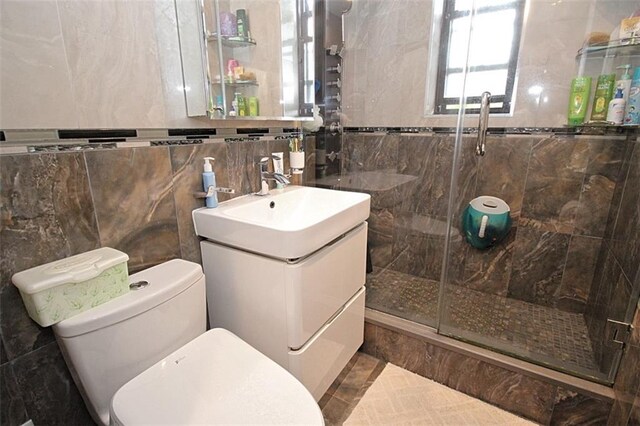 bathroom featuring vanity, a shower stall, toilet, and tile walls