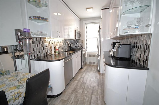 kitchen featuring stainless steel appliances, dark countertops, a sink, decorative backsplash, and light wood-type flooring
