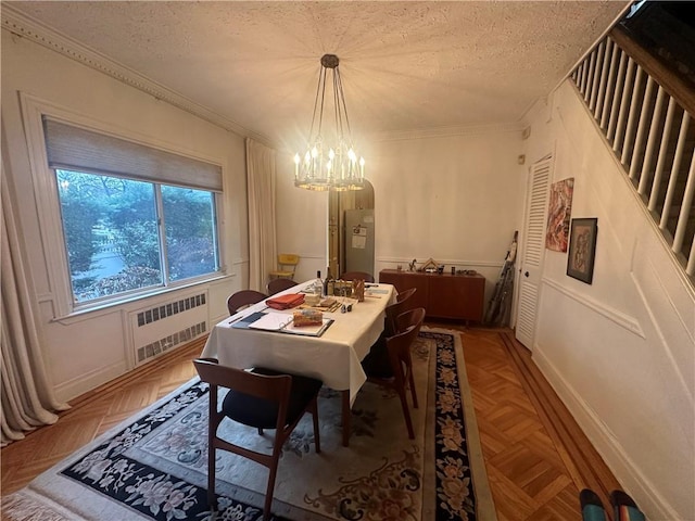 dining room with parquet flooring, a textured ceiling, ornamental molding, a notable chandelier, and radiator heating unit