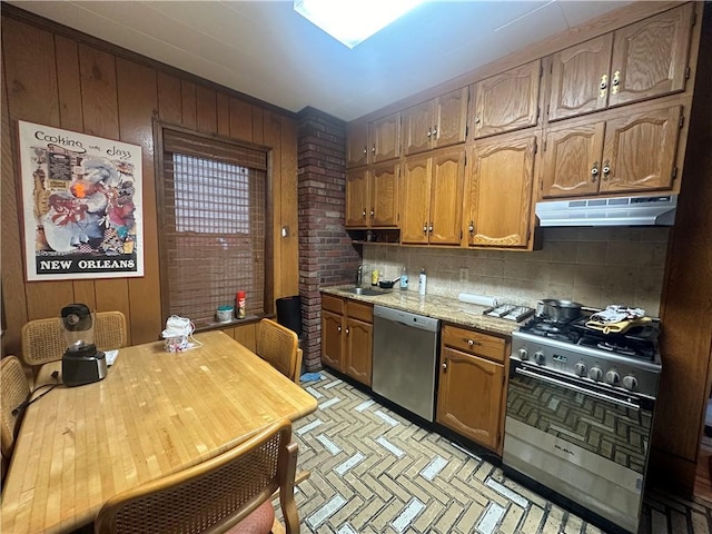 kitchen featuring sink, wooden walls, appliances with stainless steel finishes, tasteful backsplash, and light stone counters