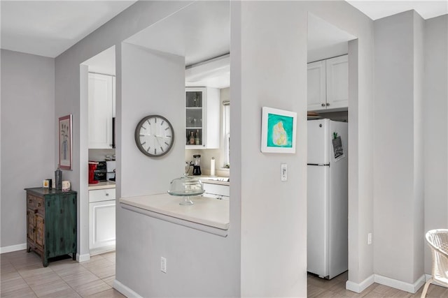 kitchen with baseboards, white cabinets, glass insert cabinets, freestanding refrigerator, and light countertops