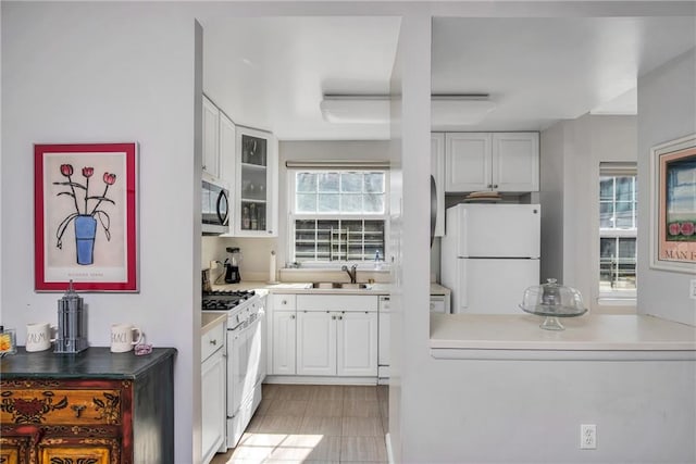 kitchen with white appliances, glass insert cabinets, white cabinets, and a sink