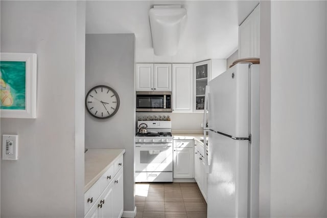 kitchen featuring white appliances, glass insert cabinets, white cabinets, and light countertops