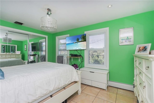 bedroom with light tile patterned floors, a closet, multiple windows, and a baseboard heating unit