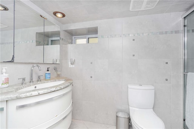 bathroom with a shower with door, vanity, tile walls, and toilet