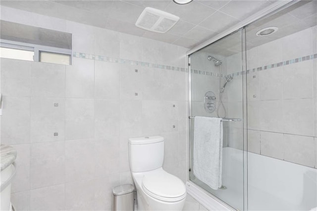 bathroom with toilet, a shower with shower door, and tile walls