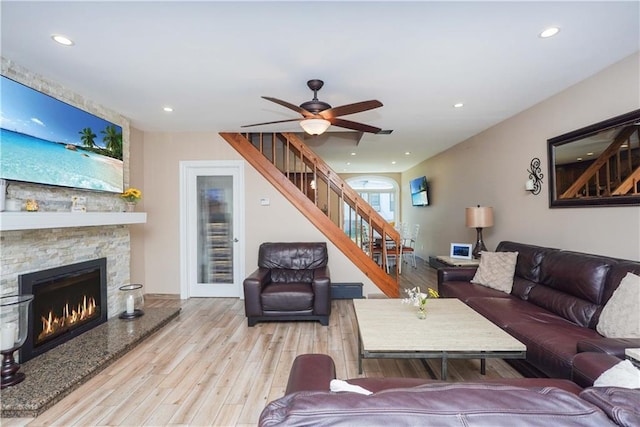 living room with ceiling fan, light hardwood / wood-style floors, and a stone fireplace