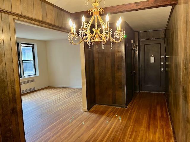 interior space featuring radiator, a notable chandelier, beam ceiling, and wood finished floors