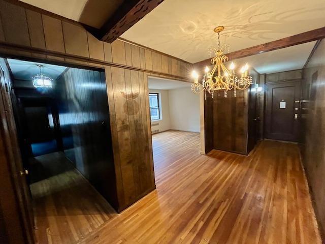 interior space featuring light wood finished floors, beamed ceiling, wood walls, and an inviting chandelier