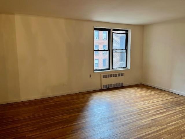 unfurnished room with baseboards, radiator heating unit, and wood finished floors