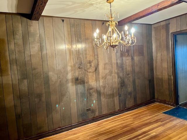 spare room featuring a notable chandelier, wooden walls, beam ceiling, and wood finished floors