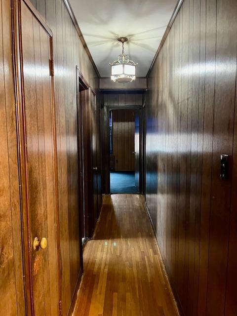 corridor with a notable chandelier, wood walls, crown molding, and hardwood / wood-style floors