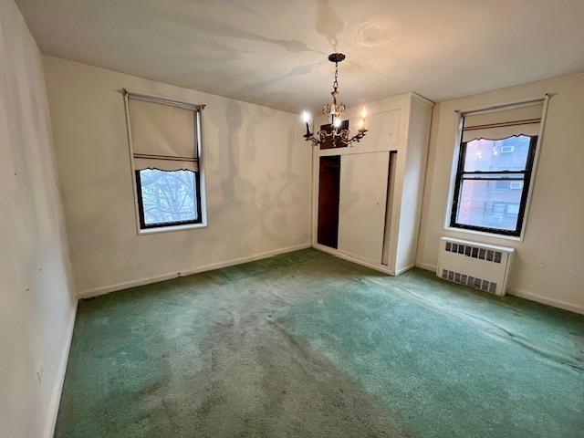 spare room featuring carpet floors, baseboards, radiator heating unit, and an inviting chandelier