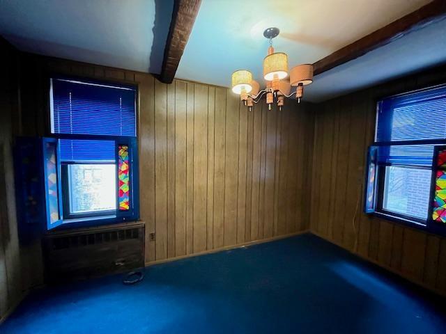 spare room featuring a notable chandelier, beamed ceiling, and wooden walls