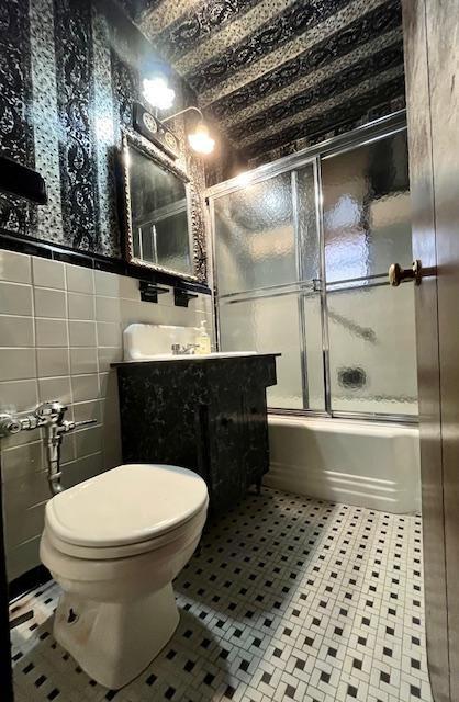 full bath with enclosed tub / shower combo, toilet, vanity, tile walls, and tile patterned floors