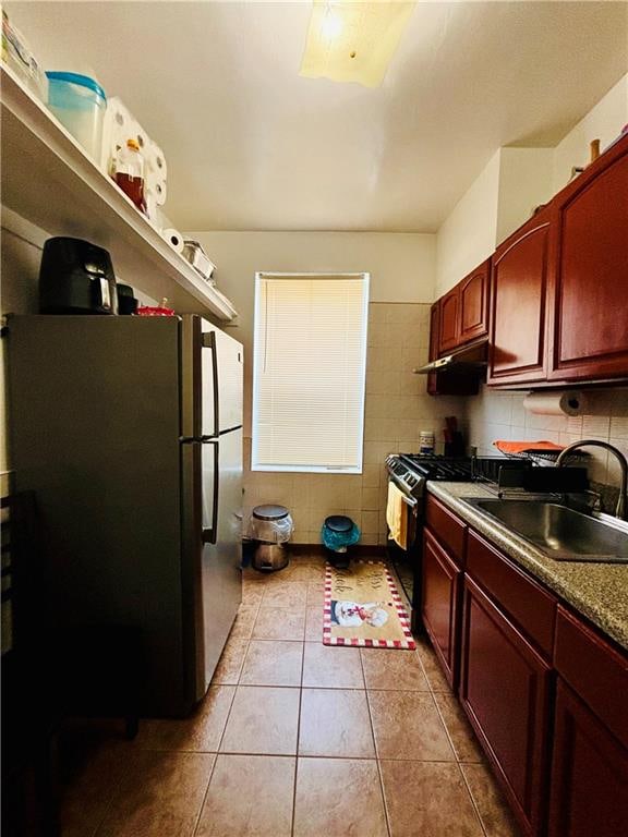 kitchen with backsplash, stainless steel refrigerator, light tile patterned floors, sink, and stove