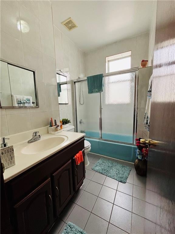 full bathroom with toilet, tile walls, tile patterned floors, bath / shower combo with glass door, and vanity