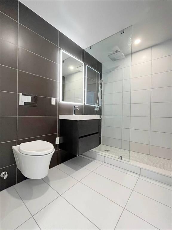 bathroom featuring toilet, tiled shower, tile patterned flooring, tile walls, and vanity